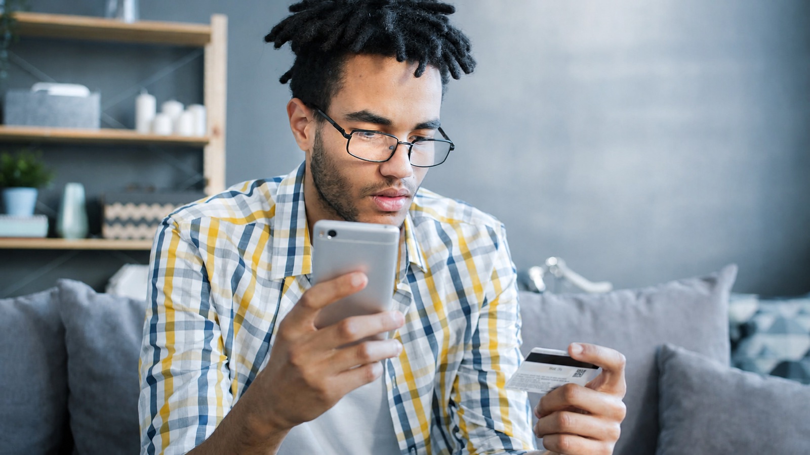 Mann prüft beim Onlinekauf eine Kreditkarte am Smartphone